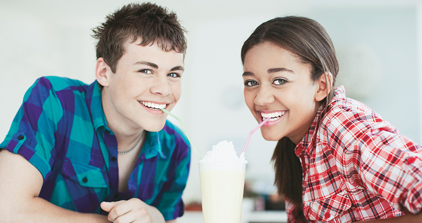 Two teens who have had wisdom teeth removal smile while sharing a milkshake