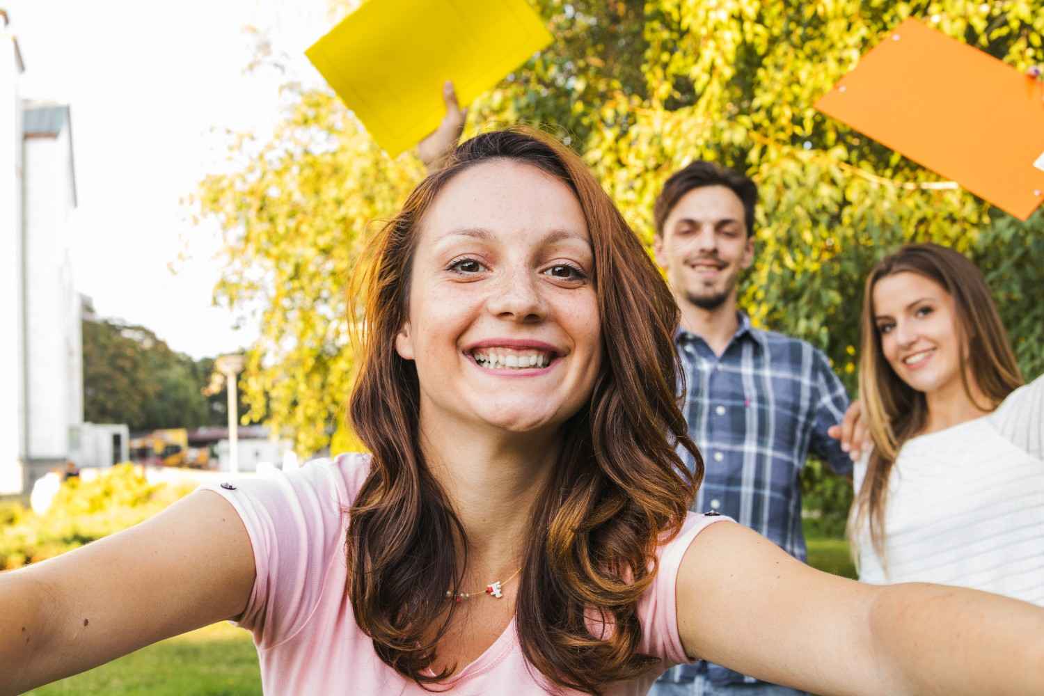 Smiling woman taking a selfie outdoors with friends in the background.